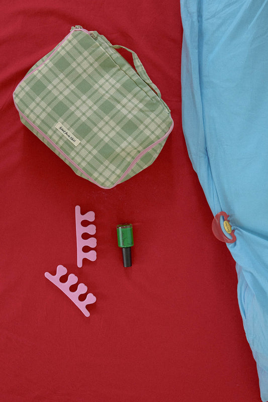 Hotel827 cotton travel pouch in small Evergreen on a red fabric surface next to a light blue sheet.