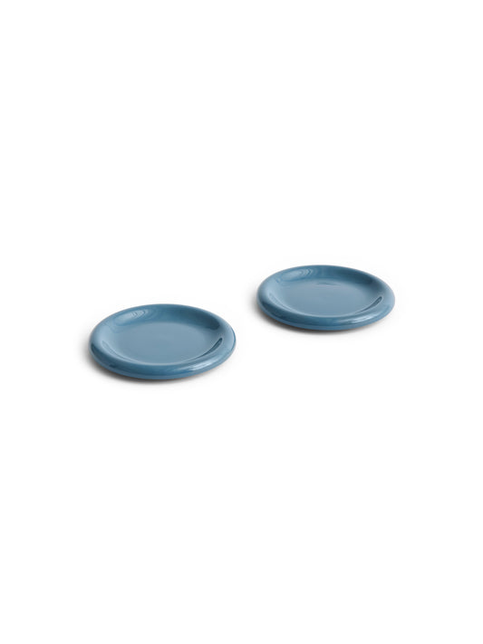 Side angle of two HAY Barro terracotta 18cm plates showcasing a rich high-gloss dark blue glaze and distinctive natural rolled edges.