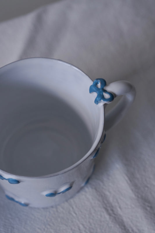 Close up of CARRON Paris handmade white ceramic Nœud-Nœud Trianon mug featuring a hand-painted sky blue bow handle detail