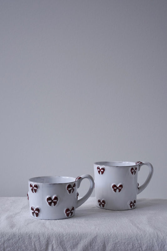 CARRON Paris handmade white ceramic Nœud-Nœud Trianon mug featuring a hand-painted deep bordeaux bow handle detail, in small and medium sizes.