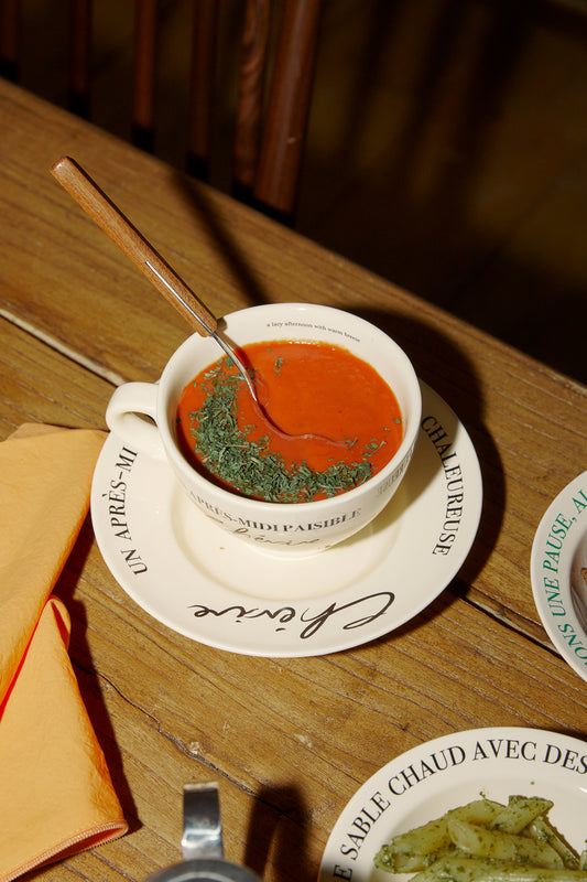 Hotel Paris Chill Lazy Vibe Coffee Cup in Black serving a tomato soup on the Lazy Vibe side plate on a wooden table.