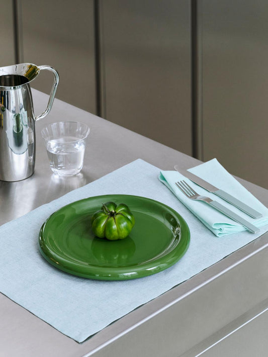 Green 24cm HAY Barro terracotta dinner plate on a bluish grey table cloth on a stainless steel bench top.