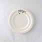 A pack shot of Studio M' Myrtille Dessert Plate in warm cream ceramic, featuring a gently rippled edge and a hand-painted, thickly glazed vintage blueberry and leaf motif.