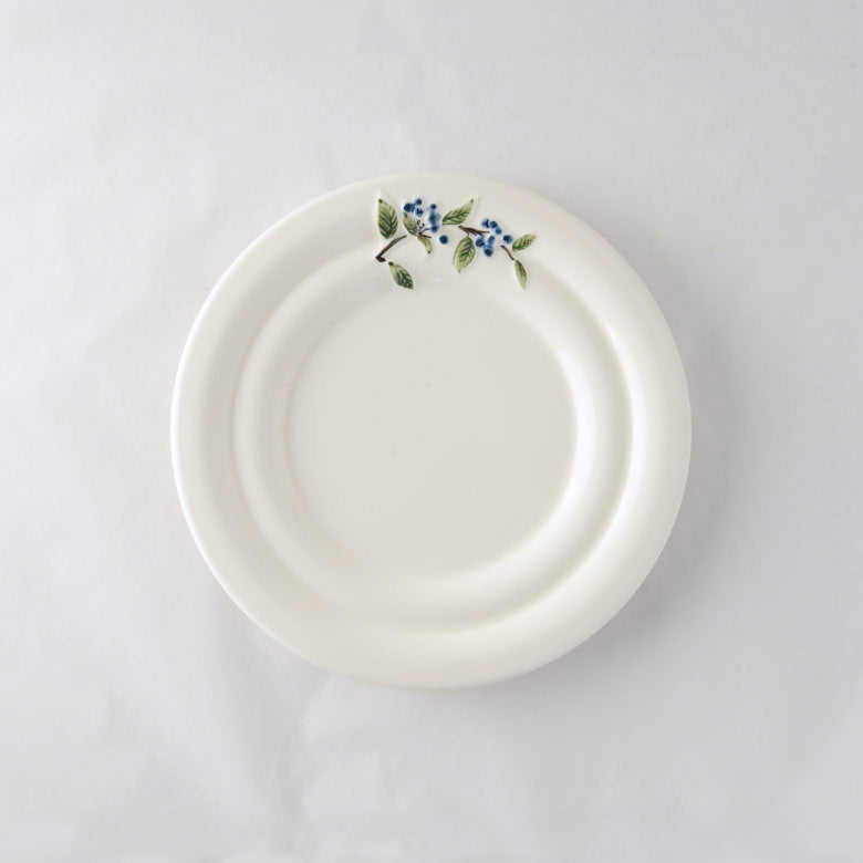 A pack shot of Studio M' Myrtille Dessert Plate in warm cream ceramic, featuring a gently rippled edge and a hand-painted, thickly glazed vintage blueberry and leaf motif.