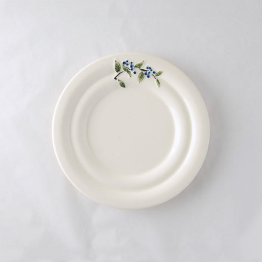 A pack shot of Studio M' Myrtille Dessert Plate in warm cream ceramic, featuring a gently rippled edge and a hand-painted, thickly glazed vintage blueberry and leaf motif.