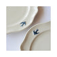A close-up shot of the hand painted bird on the rim of Studio M' Early Bird Oval Plate L.