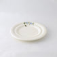 A pack shot of Studio M' Myrtille Dessert Plate in warm cream ceramic, from a side angle.