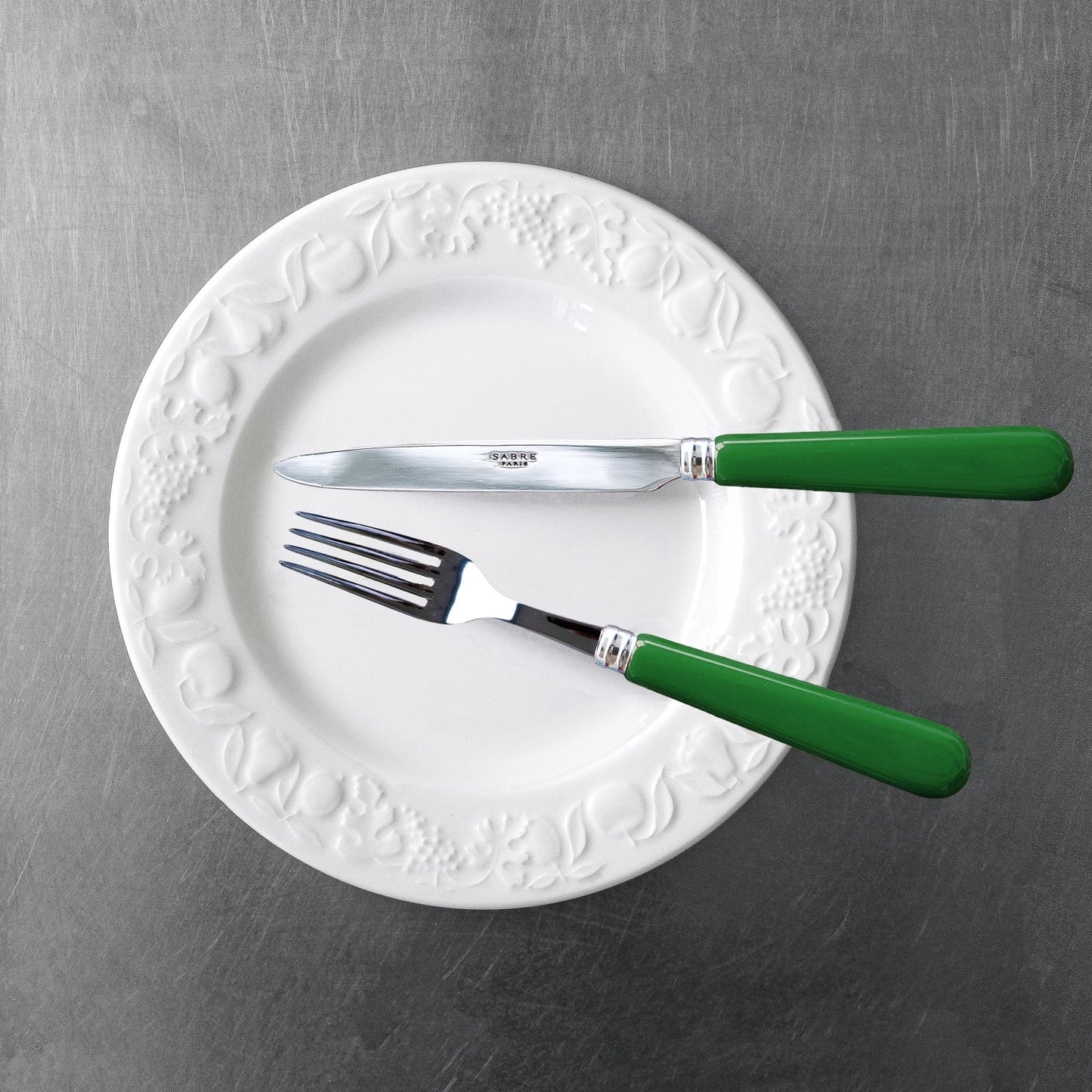 Sabre Paris Pop Unis cake fork in Green on a white dish on the stainless steel benchtop. 