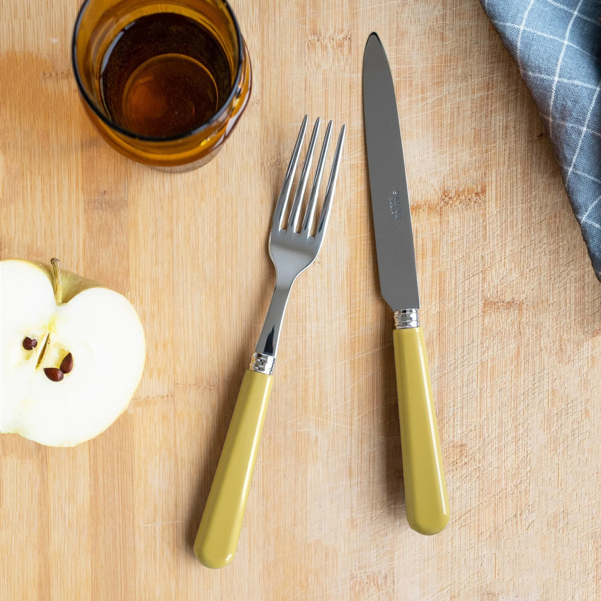 Sabre Paris Pop cutlery set in yellow corn on a cutting board next to a tumbler.