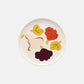 Overhead view of the Marimekko Oiva 20cm white stoneware plate featuring the Kukasta Kukkaan abstract floral and leaf pattern in terracotta, vanilla, and plum.