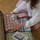 A woman packing Hotel827 cotton travel pouches into a suitcase on a wooden floor. 