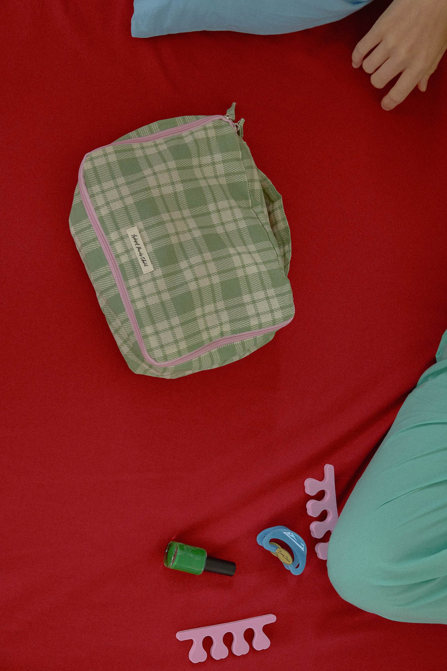 Hotel827 small travel pouch in evergreen lies on a red blanket.