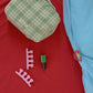 Hotel827 cotton travel pouch in small Evergreen on a red fabric surface next to a light blue sheet. 
