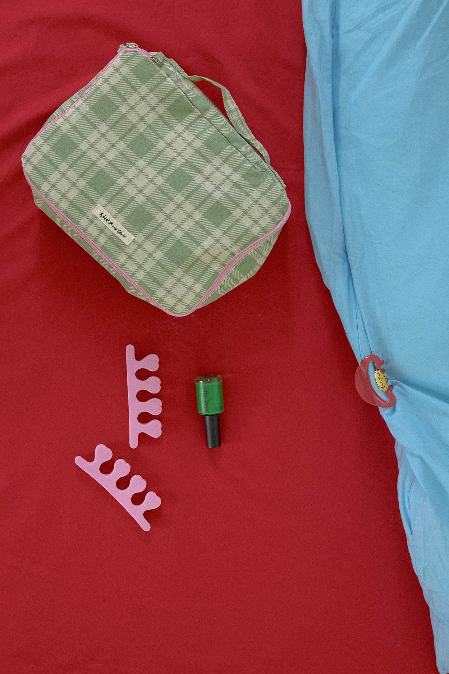 Hotel827 cotton travel pouch in small Evergreen on a red fabric surface next to a light blue sheet. 