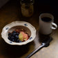 Studio M' Early Bird 170 porcelain bowl featuring a hand-painted blue swallow relief on a scalloped floral rim, used as a cereal bowl and paired with an earthy style coffee mug. 