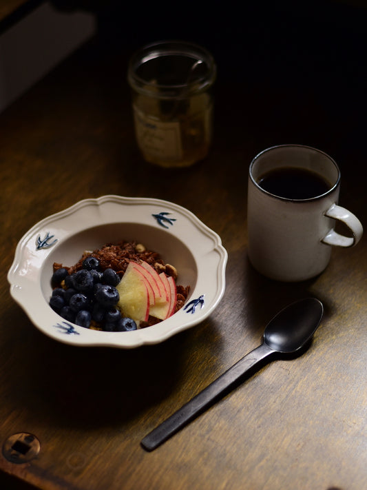 Studio M' Early Bird 170 porcelain bowl featuring a hand-painted blue swallow relief on a scalloped floral rim, used as a cereal bowl and paired with an earthy style coffee mug. 