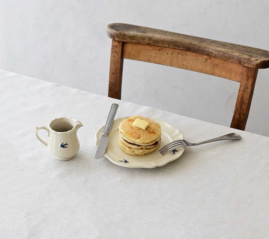 Studio M Early Bird small creamer next to a plate of pancakes on a white table cloth.
