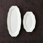 A comparison photo of Studio M Ornata matte white 20cm and 30cm oval plates on a brown metal surface. 