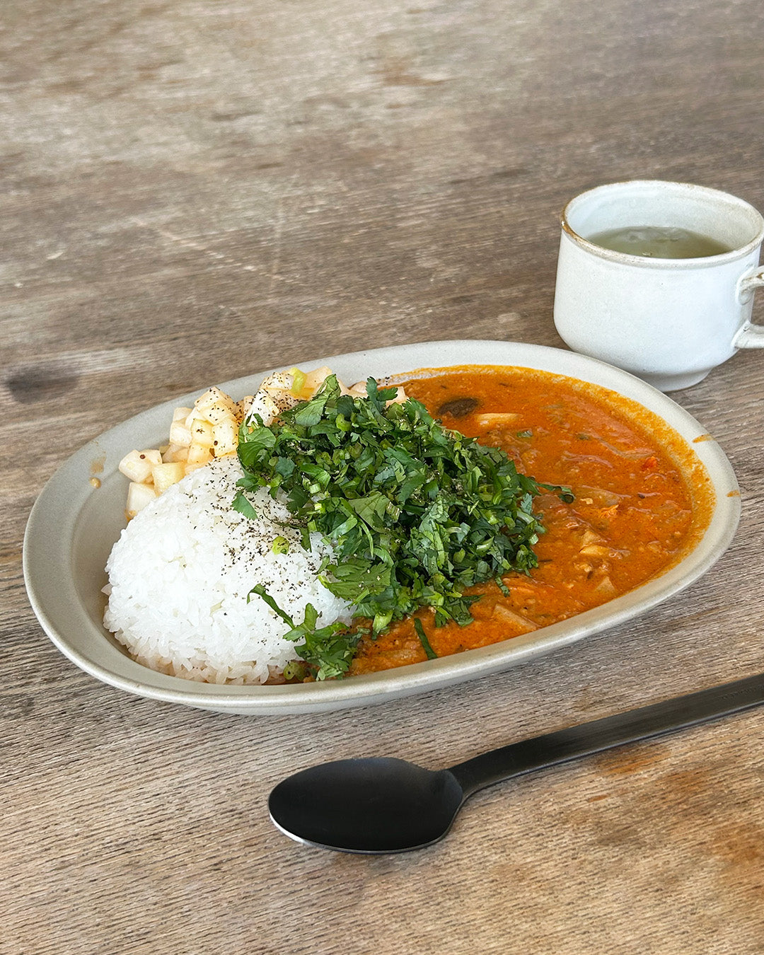 Studio M Karil 25cm oval earthenware plates in ecru colour serving curry and rice on a wooden table.