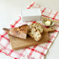 Studio M Japanese solid walnut cutting board collection in oblong medium size, serving cut baguette on a tea towel. 
