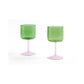 Side-angle view of a set of two HAY Tint Wine Glasses, showcasing minimalist green borosilicate glass bowls resting on delicate stems in light pink. 