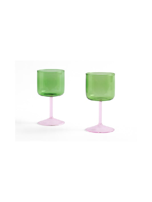 Side-angle view of a set of two HAY Tint Wine Glasses, showcasing minimalist green borosilicate glass bowls resting on delicate stems in light pink. 