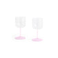 Side-angle view of a set of two HAY Tint Wine Glasses, showcasing minimalist clear borosilicate glass bowls resting on delicate stems in jade light pink and light pink.