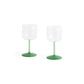 Side-angle view of a set of two HAY Tint Wine Glasses, showcasing minimalist clear borosilicate glass bowls resting on delicate stems in jade light green and jade dark green.