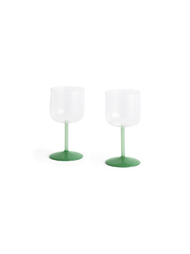Side-angle view of a set of two HAY Tint Wine Glasses, showcasing minimalist clear borosilicate glass bowls resting on delicate stems in jade light green and jade dark green.