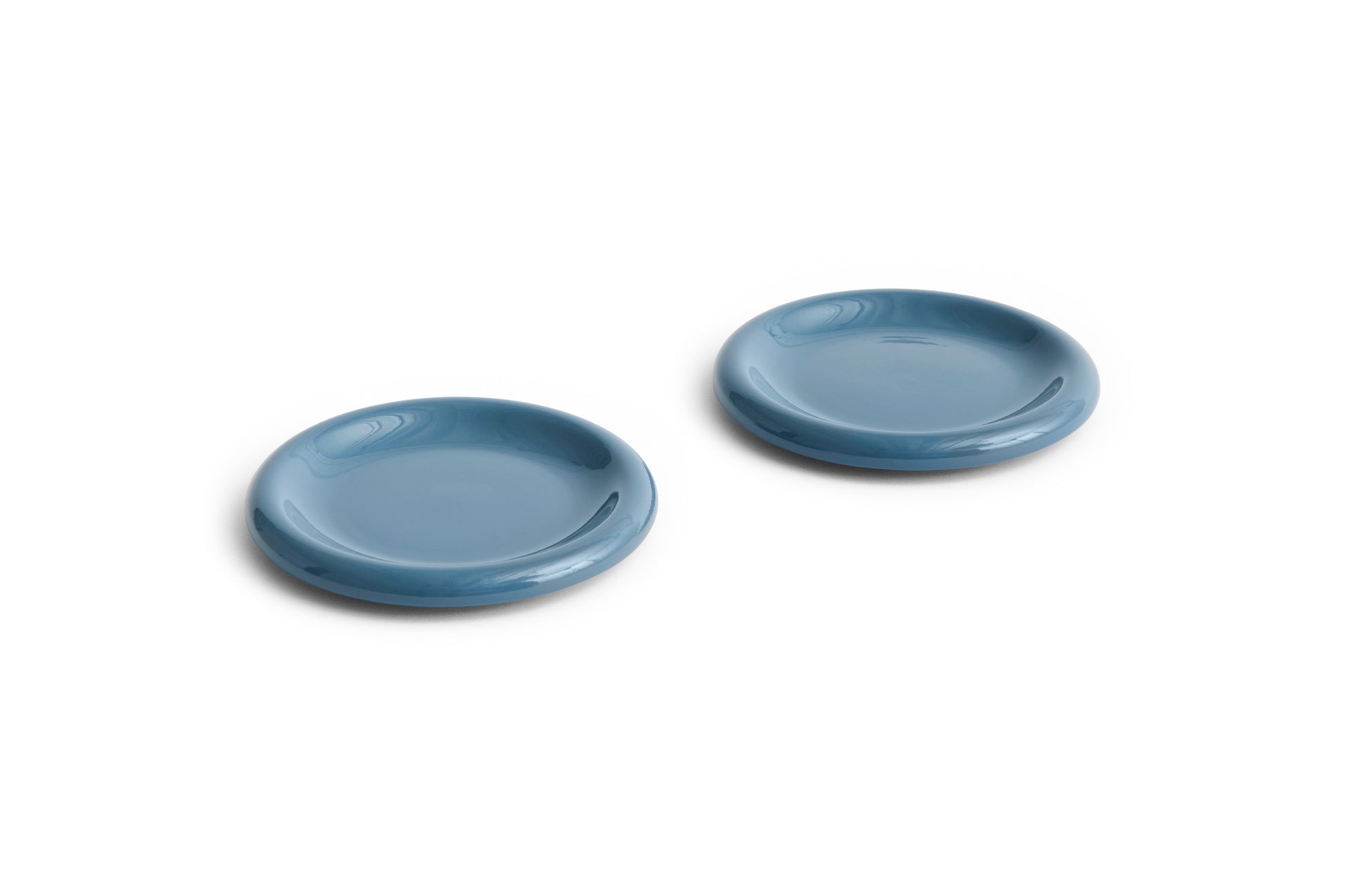 Overhead angle of two HAY Barro terracotta 18cm plates showcasing a rich high-gloss dark blue glaze and distinctive natural rolled edges.
