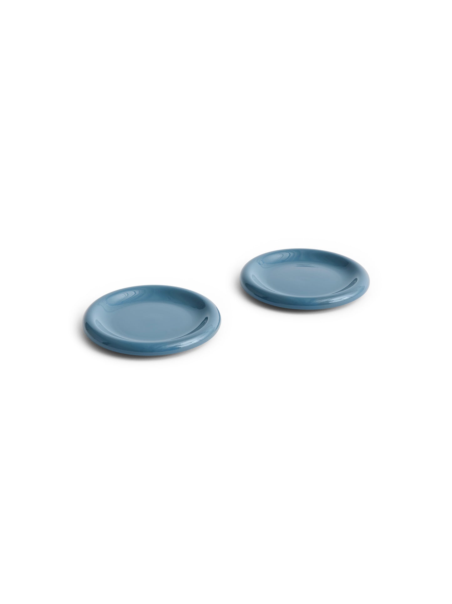 Side angle of two HAY Barro terracotta 18cm plates showcasing a rich high-gloss dark blue glaze and distinctive natural rolled edges.
