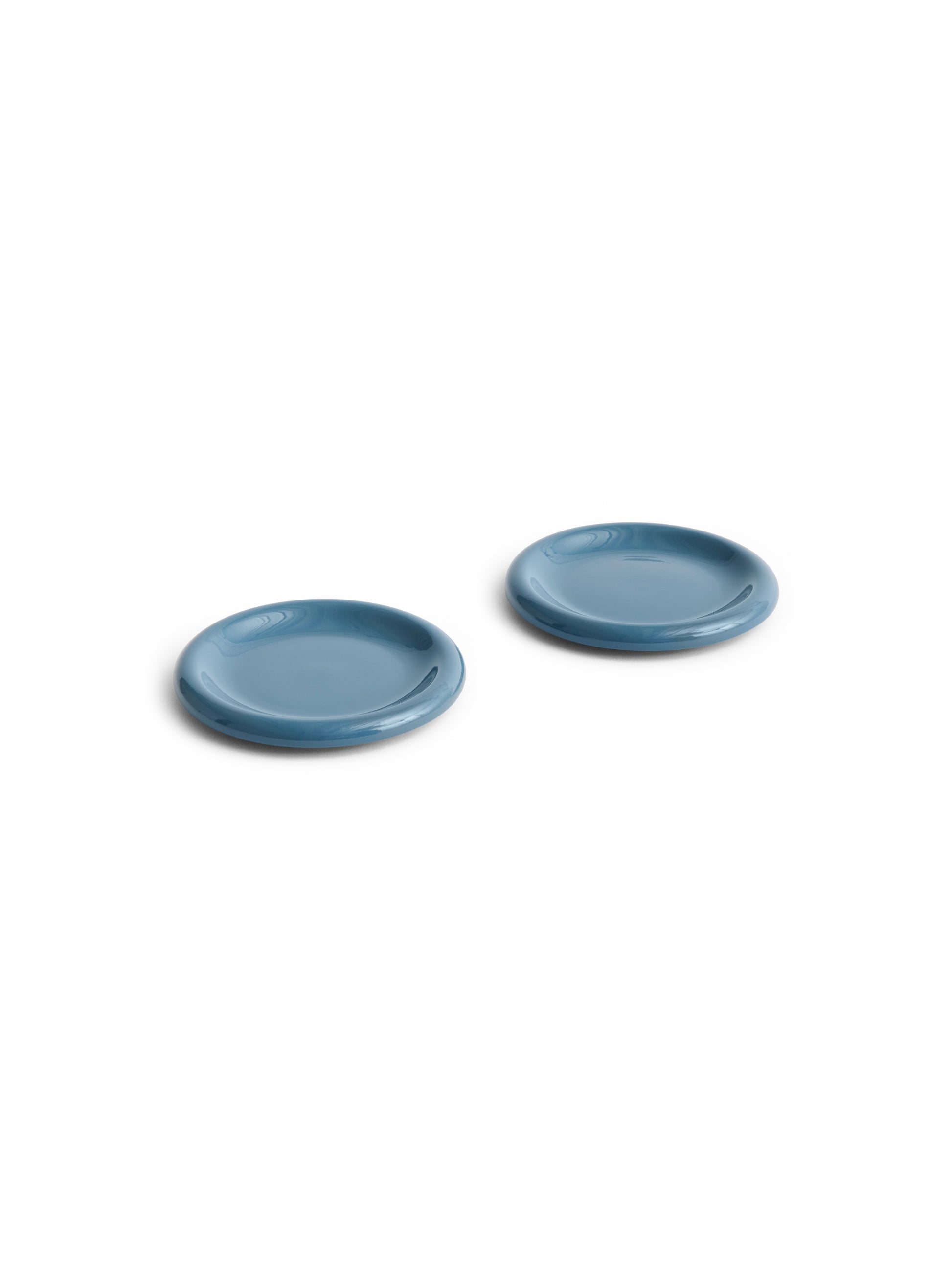 Side angle of two HAY Barro terracotta 18cm plates showcasing a rich high-gloss dark blue glaze and distinctive natural rolled edges.