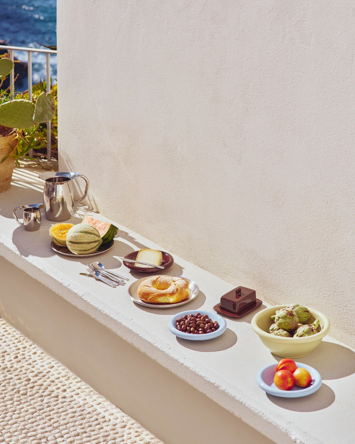 A modern outdoor setting featuring a set of two light blue glazed terracotta HAY Barro bowls and othe Hay tableware products.