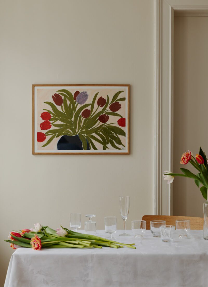 A lifestyle shot of Art print  Tulips in a Blue Vase by Anine Cecilie Iversen with a table setting of wine glasses and tulips.