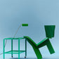 Hay Apex Desk Lamp in Emerald Green on a side table styled with a green chair and a stool.
