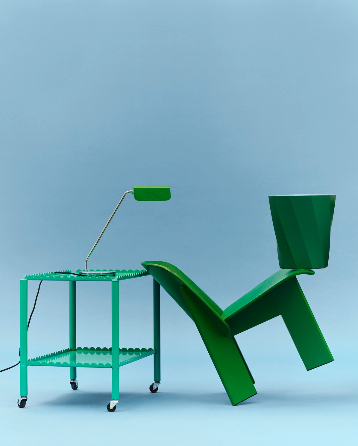 Hay Apex Desk Lamp in Emerald Green on a side table styled with a green chair and a stool.
