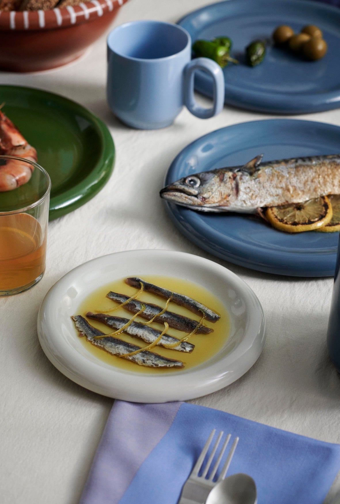 Dinner table with Hay Barro plates of food, including fish, on a white tablecloth.