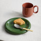 Hay Barro Plate 18cm in Green paired with an orange mug at breakfast.
