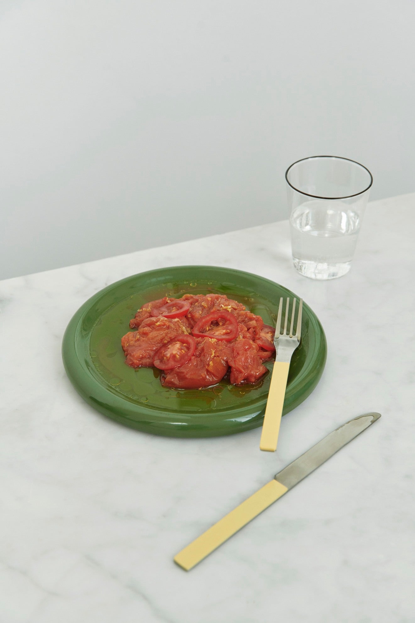Hay Barro plate 18cm in Green with smashed tomotoes, yellow fork and knife on a white tablecloth.