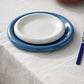 A close-up view of 18cm Hay Barro plate in off-white stacked on 24cm HAY Barro terracotta dinner plate in dark blue. 