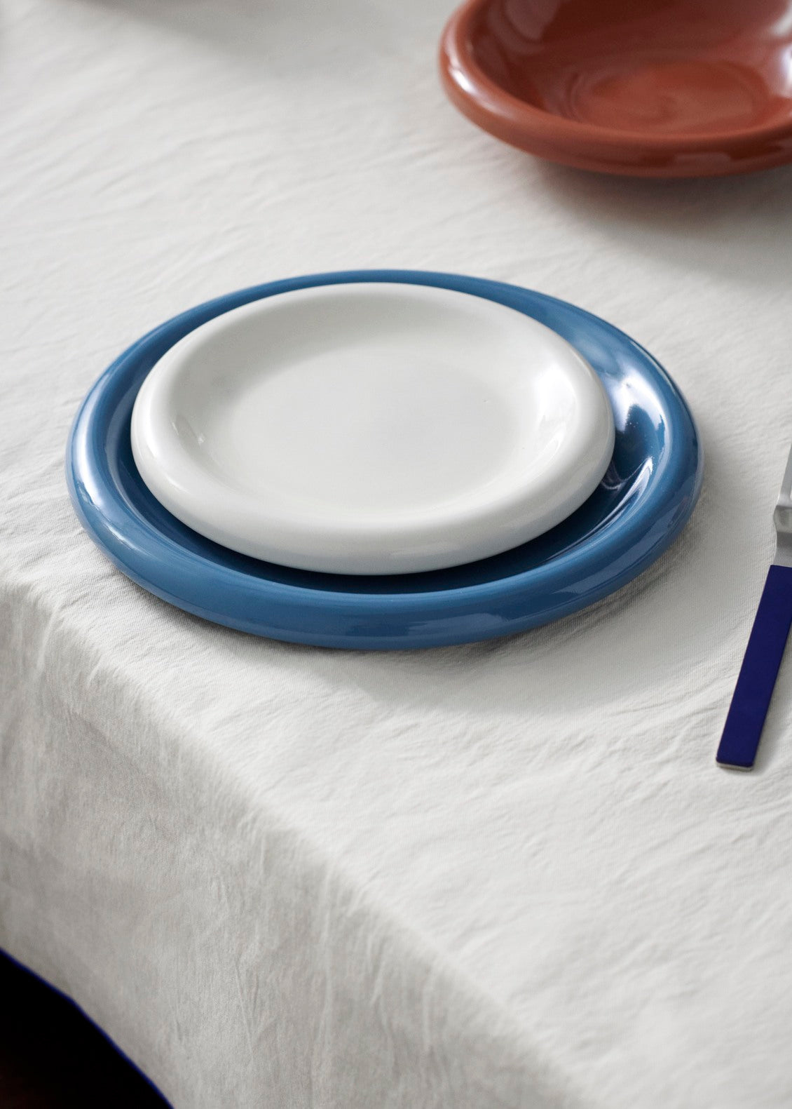A close-up view of 18cm Hay Barro plate in off-white stacked on 24cm HAY Barro terracotta dinner plate in dark blue. 