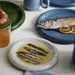 Dinner table with HAY Barro Plate 18cm in Off-White of food, including fish, on a white tablecloth.