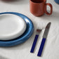 Dinnerware set with Hay Barro Plate 18cm in Off-White stacked on top of the Barro Plate 24cm in Dark Blue, red mug, fork, and knife on a white table cloth.