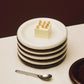 Stacked Hay 18cm Barro plates in off-white and brown, serving a cake on a white surface. 