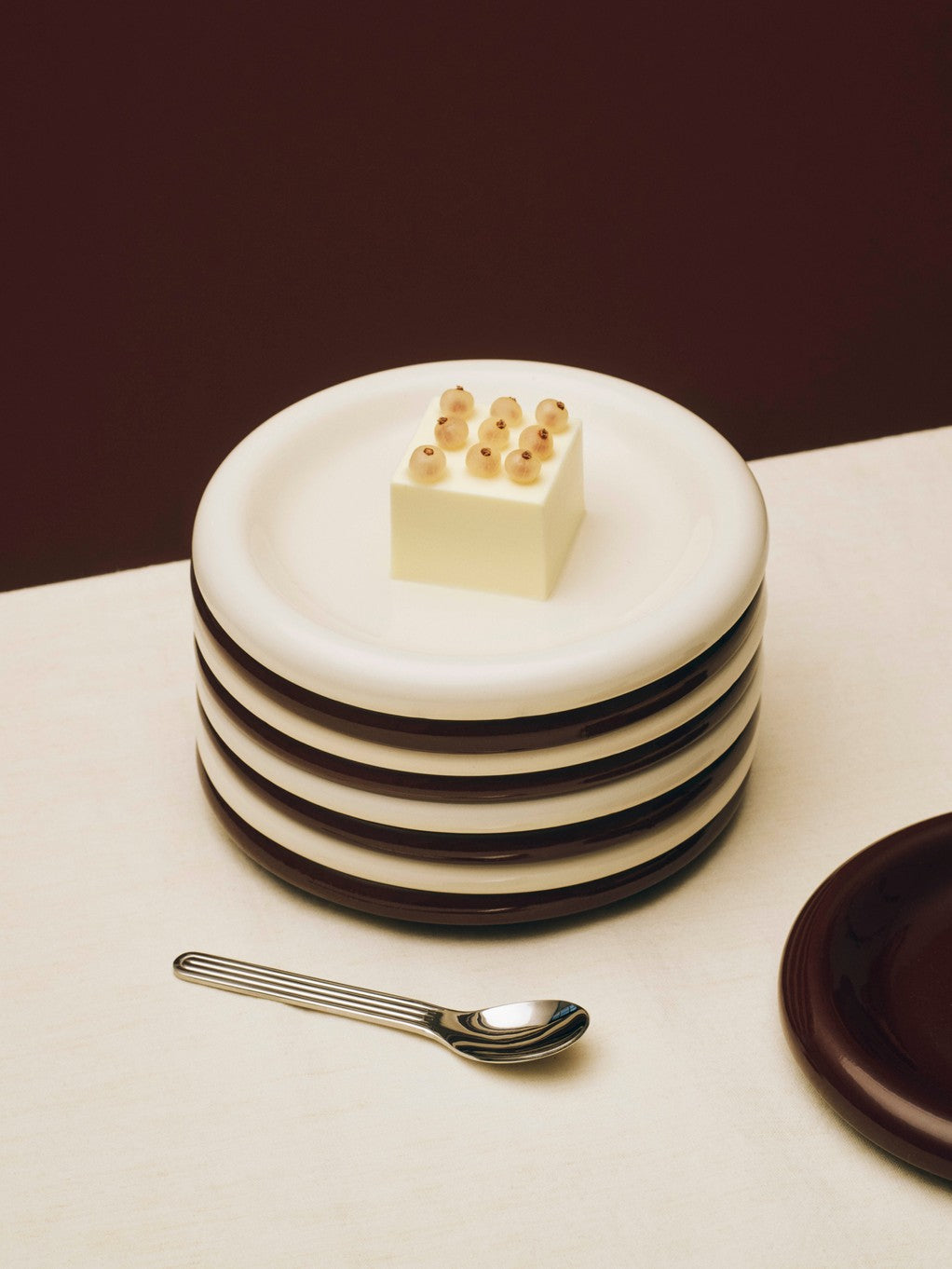 Stacked Hay 18cm Barro plates in off-white and brown, serving a cake on a white surface. 