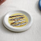 HAY Barro Plate 18cm in Off-White with anchovies in a light sauce on a white surface