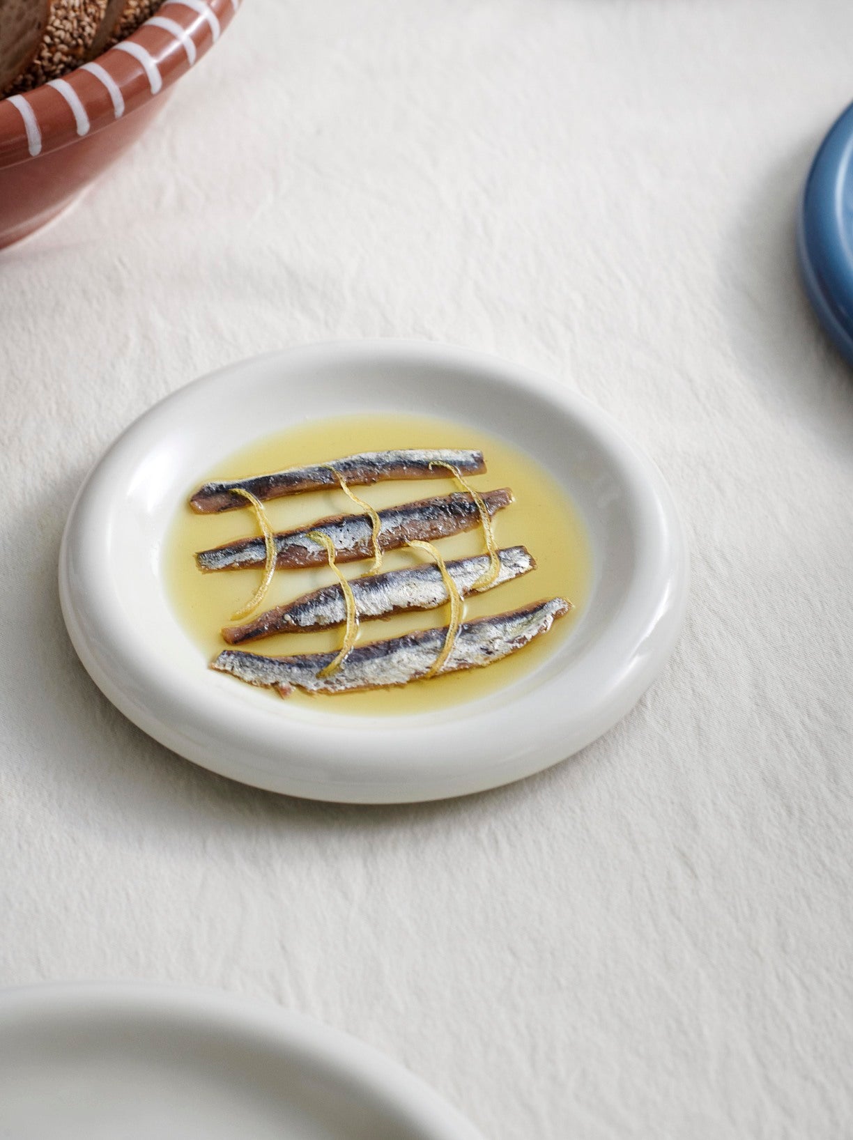 HAY Barro Plate 18cm in Off-White with anchovies in a light sauce on a white surface