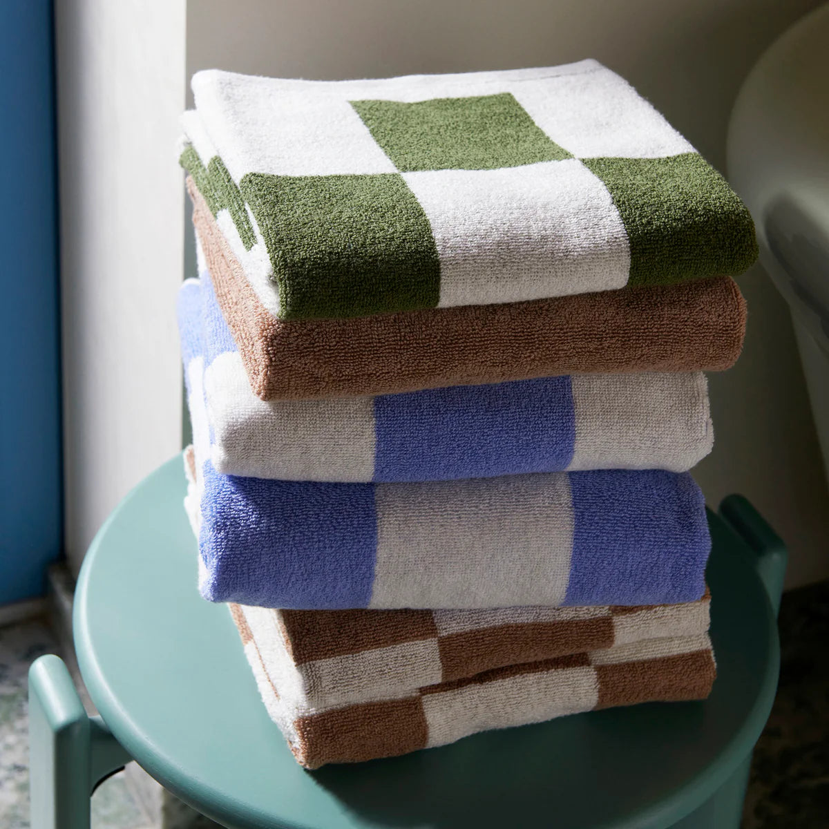 Stack of Hay Check Wash Clothes in green, brown, blue, and beige on a green chair.