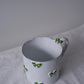Close-up of CARRON Paris handmade white ceramic Nœud-Nœud Trianon mug featuring a hand-painted leaf green bow handle detail.