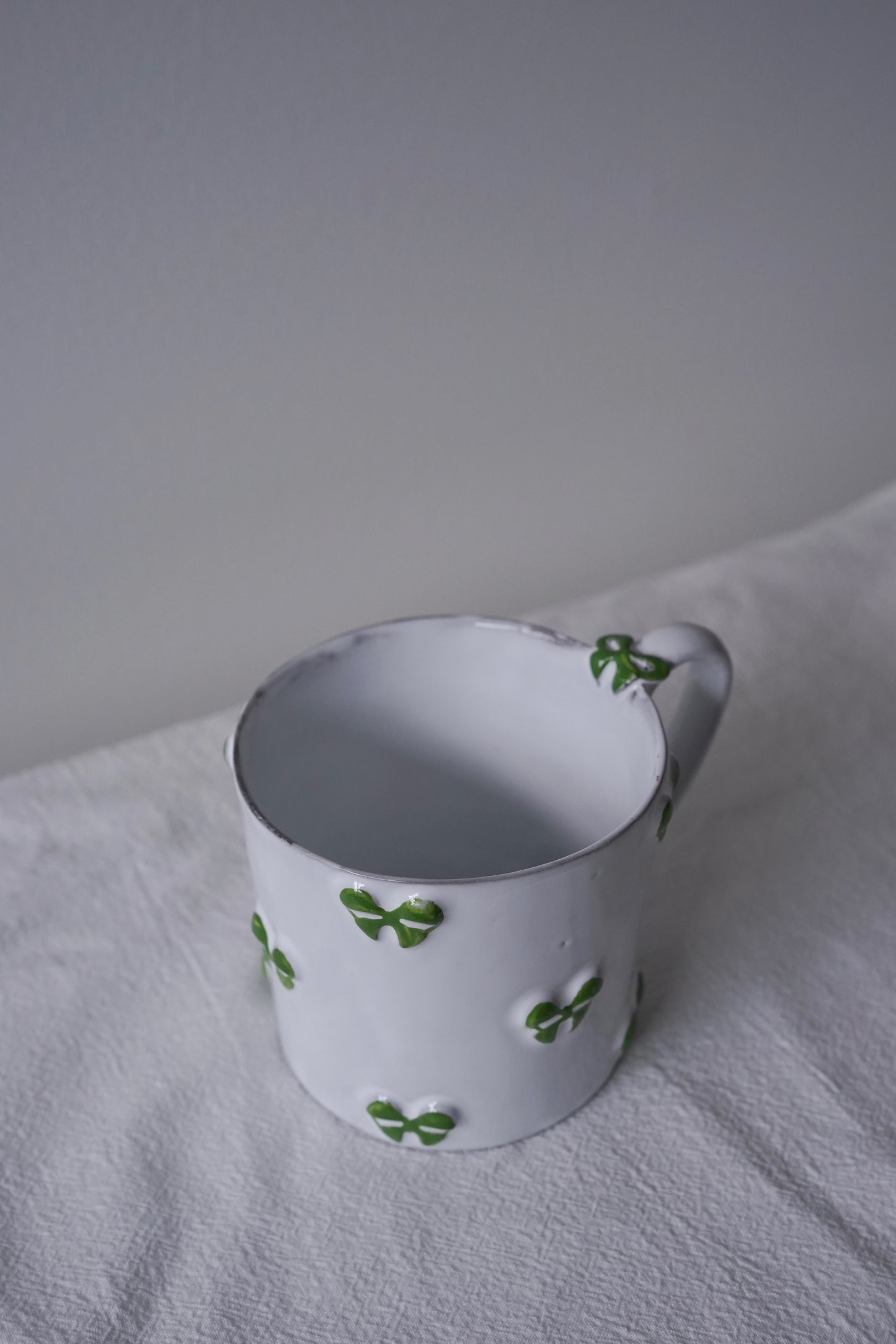 Close-up of CARRON Paris handmade white ceramic Nœud-Nœud Trianon mug featuring a hand-painted leaf green bow handle detail.